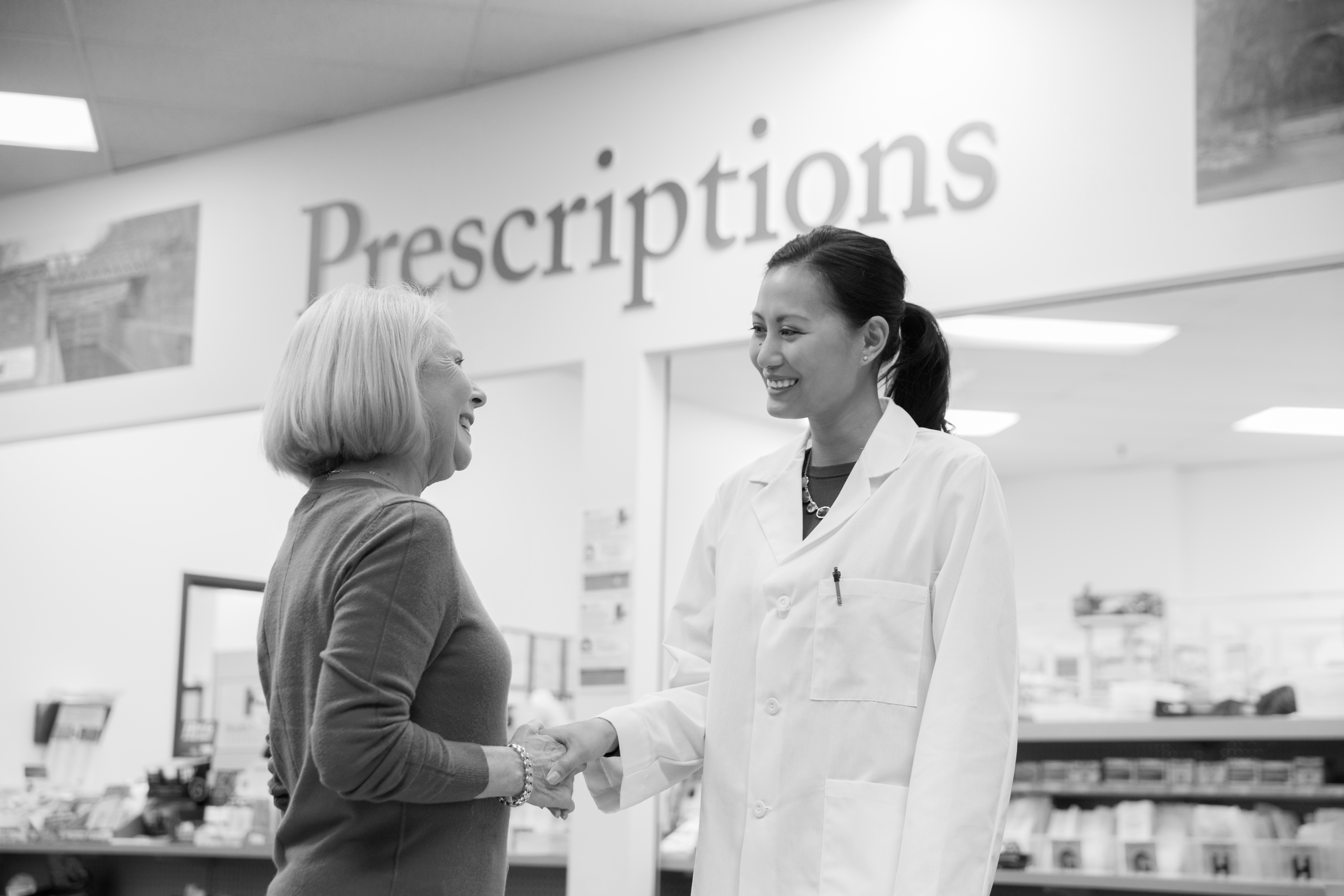 A pharmacist greets a patient in front of the pharmacy counter