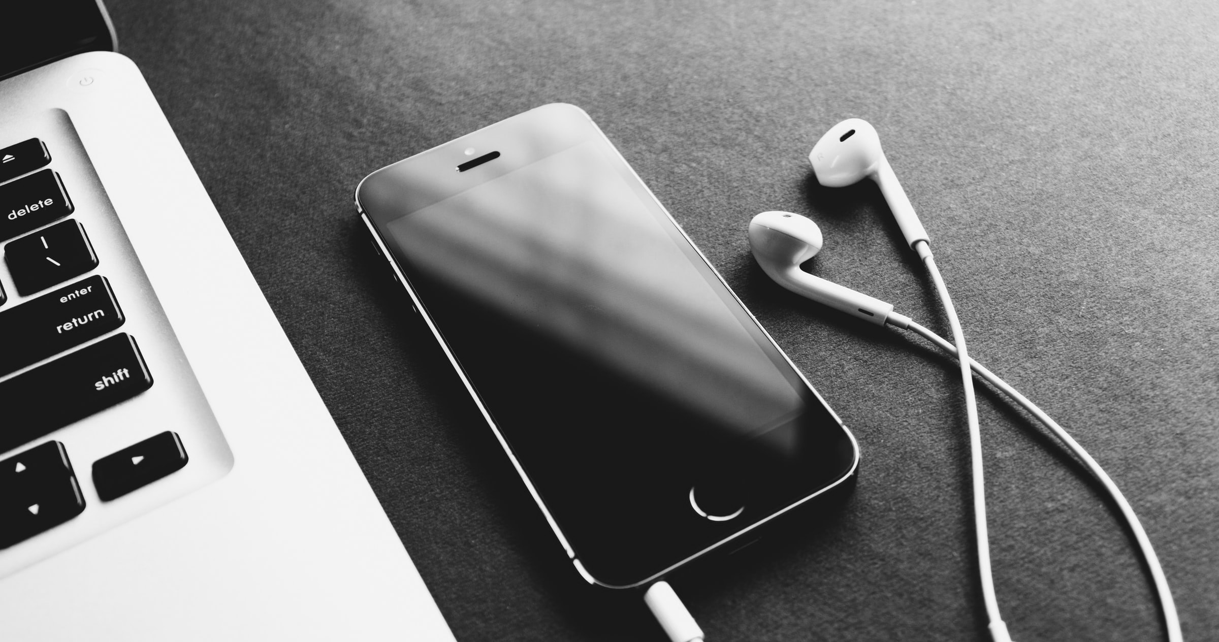 Earbud headphones connected to an iPhone next to a laptop computer
