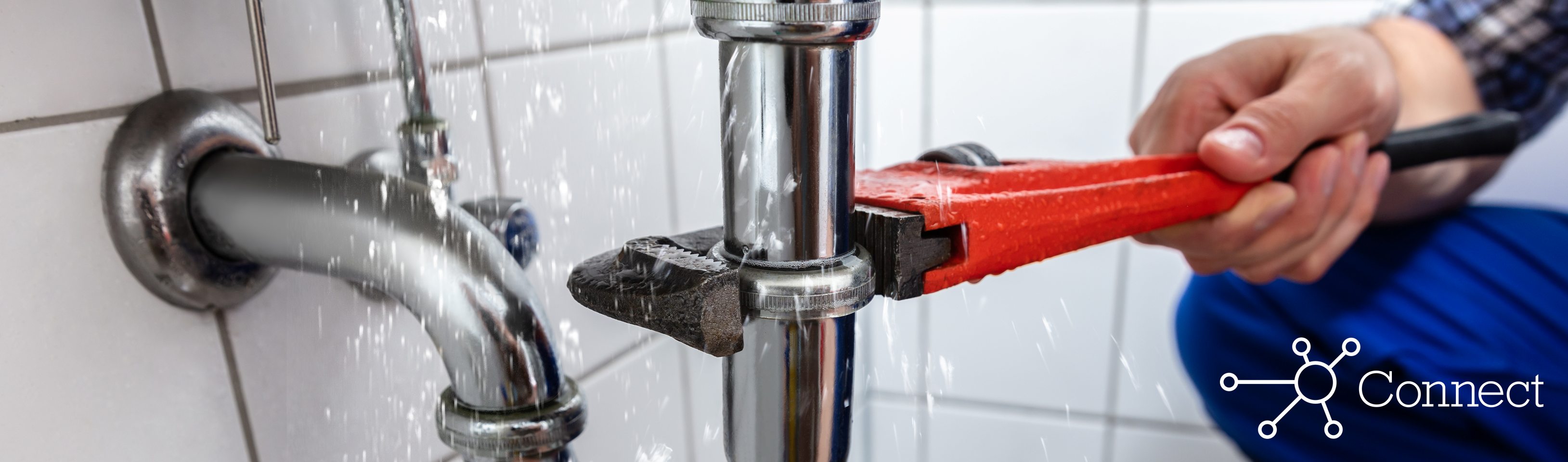 A plumber using a wrench to fix a leaking pipe under a sink